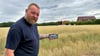 Retzaus Ortswehrleiter Peter Sommerlatte steht mit Handy und Computergrafik auf der Fläche für den Neubau des Gerätehauses. 