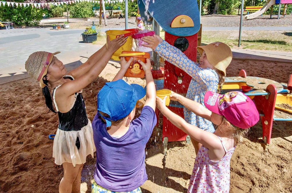 Wasserspaß und Schatten in der Kita „Pusteblume“ in Kleinkühnau. Die Kinder sind mit Sonnenschutz eingecremt und planschen im Schatten mit Wasser.