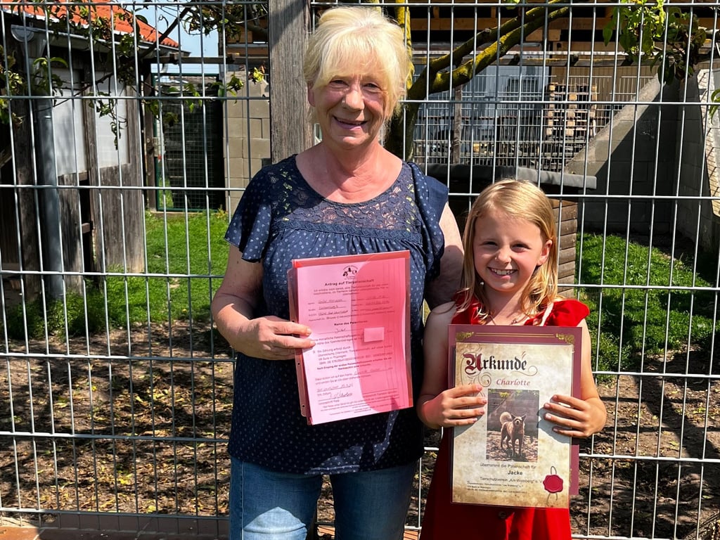 Christa Scheler, Vorsitzende des Tierschutzvereins, hält den Patenschaftsvertrag, und die achtjährige Charlotte ihre Patenschaftsurkunde in den Händen.