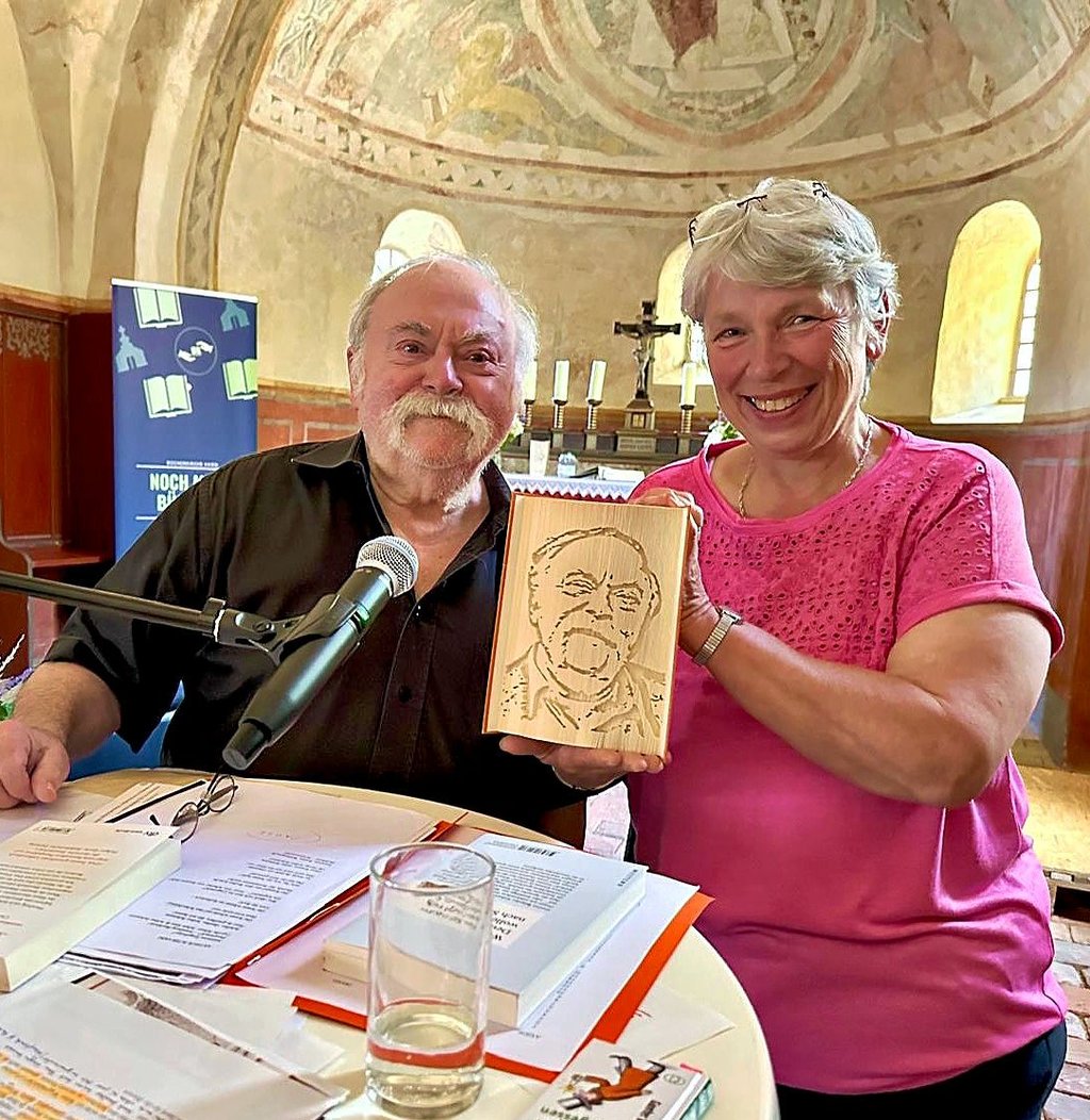 Gunter Böhnke erhält als Dank für seine zweite Benefizlesung in der Axiener Bücherkirche ein einzigartiges Buch mit Porträt überreicht.