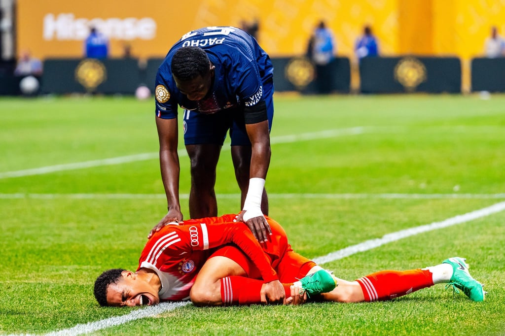 Jamal Musiala liegt mit starken Schmerzen verletzt am Boden. PSG-Profi William Pacho kümmert sich um ihn.