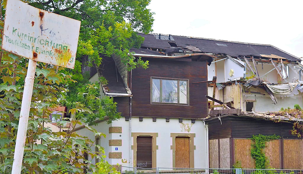 Auf dem verblichenen Schild ist die Aufschrift "Kureinrichtung Teufelsbad (Blankenburg)" zu lesen, rechts die Villa mit großen Schäden vor allem im Dachbereich.