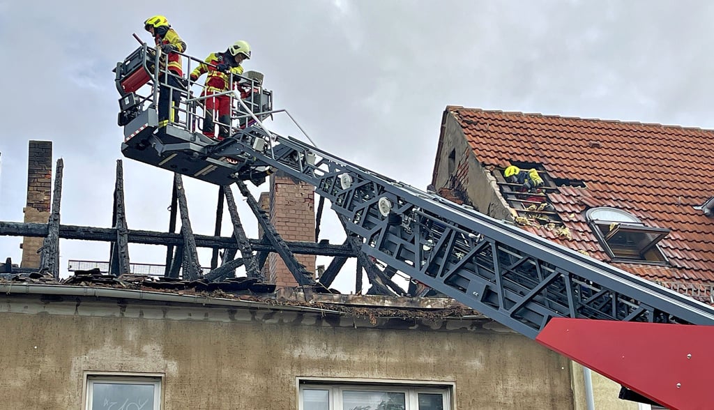 Während zwei Feuerwehrleute mit der Drehleiter das Brandobjekt sichern, bekämpft ein Kamerad Glutnester im Nachbarhaus.