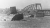 Zwei amerikanische Amphibienfahrzeuge (GMC DUKW, "Duck") auf der Grünewalder Seite. Im Hintergrund die zerstörte Elbbrücke“ im Jahr 1945.