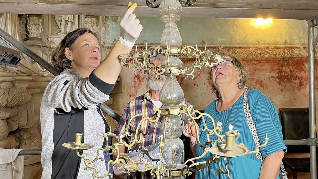 Christina Neubacher (von links), Karl Eisbein und Theresia Gebauer betrachten den Kronleuchter in der Stadtkirche von Jerichow, der für die Reinigungsarbeiten tiefer gehängt wurde, um alle Teile erreichen und dokumentieren zu können.
