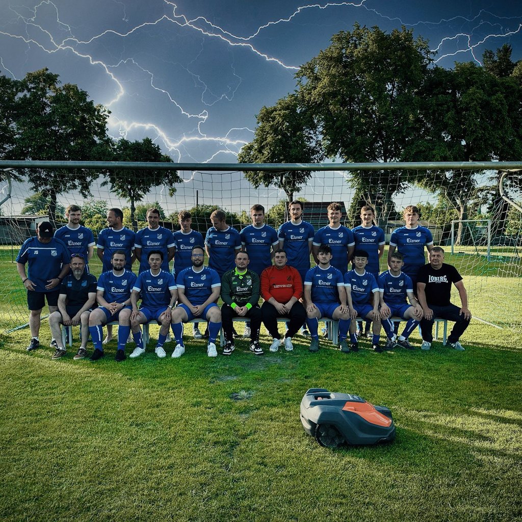 Das Team von Blau-Weiß Loburg posiert vor dem Tor – doch der Star im Vordergrund steht im Gras: Einer der beiden Mähroboter, die gestohlen wurden.