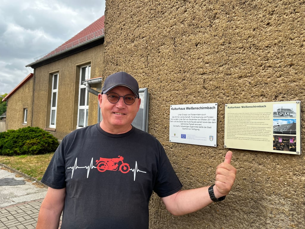 Hier zeigt Peter Hinkeldey das angebrachte Infoschild am Kulturhaus. Dieses Gebäude war früher eine Scheune und Stallanlage, bis es von Handwerkern und Genossenschaftsbauern der ehemaligen LPG „Wilhelm Pieck“ zum Kulturhaus umgebaut wurde. Die Einweihung erfolgte 1954.