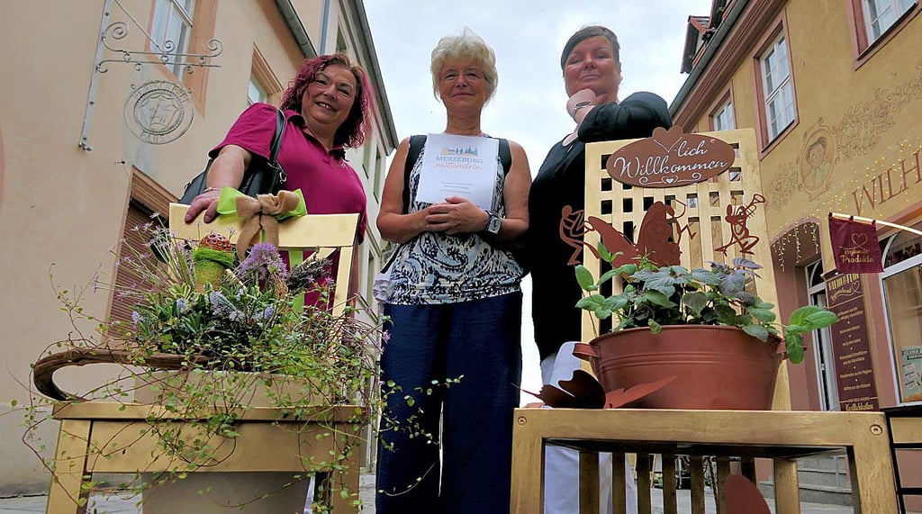Simon Funke (von l.), Christine Weigelt-Krause und Gabi Kanter haben geschmückte Stühle vor ihren Geschäften in Merseburg.