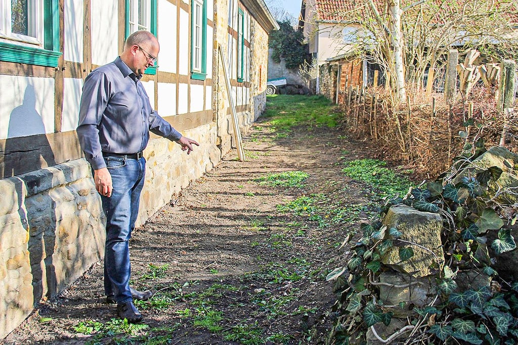 Rainer Siedekum zeigt auf die Stelle, hinter seinem Haus wo er im vergangenen Jahr einen Haarriss in der Trinkwasserleitung lokalisiert hatte. Für das austretende und versickerte Wasser musste er auch Abwassergebühren zahlen.