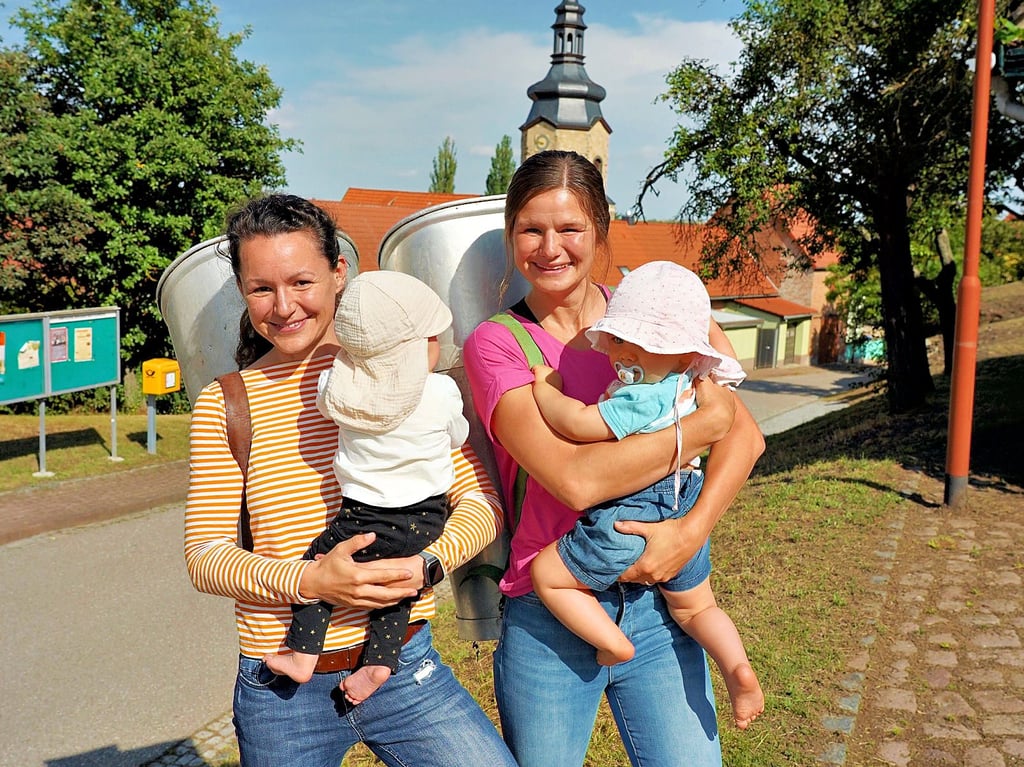 Josephine Erfurt (l. mit Töchterchen Luise) und Marianne Stock (mit Tilda) stehen an der Buttenlauf-Strecke in der Ortsmitte mit Dorndorfs Kirche.