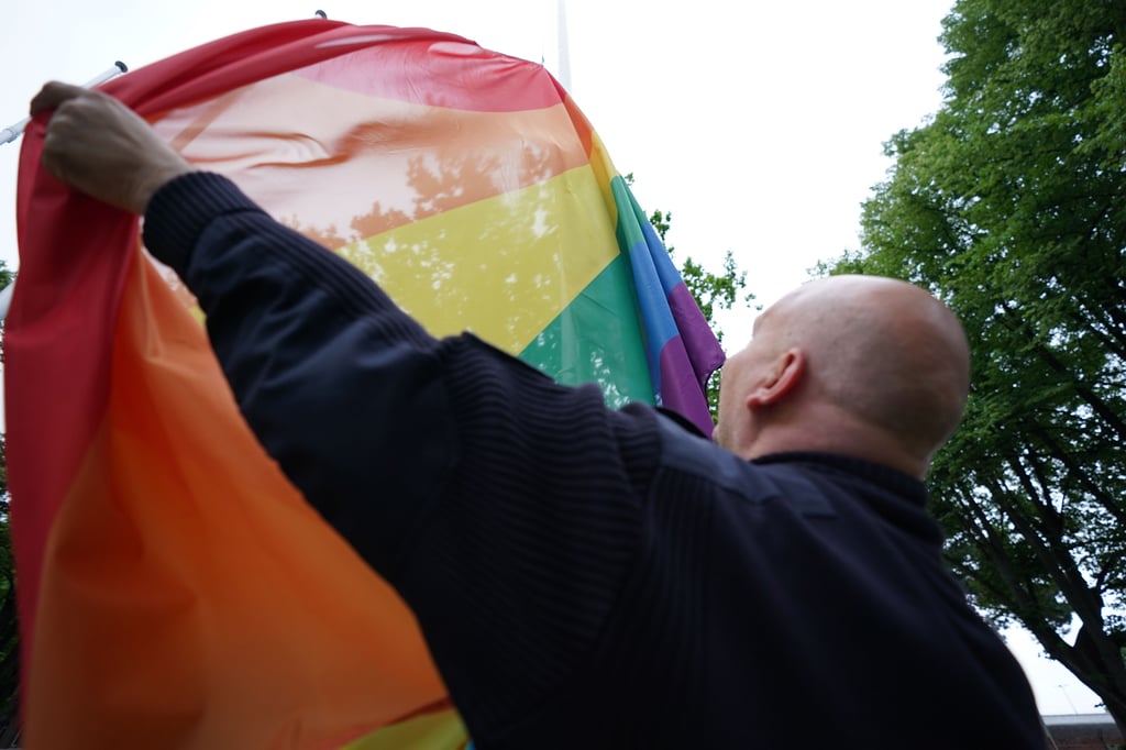 Ein Justizvollzugsbeamter hisst die Regenbogenfahne vor einem Hamburger Gefängnis. Rechte qeerer Gefangener werden öffentlich kontrovers debattiert.