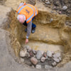 Götz Alper, Archäologe vom Landesamt für Denkmalpflege und Archäologie Sachsen-Anhalt, zeigt auf einer Grabungsfläche in Wolmirstedt auf Tonscherben, die neben Steinen in einer Kochgrube kaum zu sehen sind.