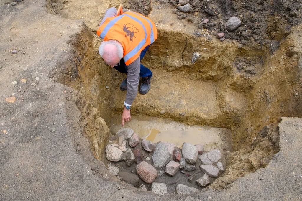 Götz Alper, Archäologe vom Landesamt für Denkmalpflege und Archäologie Sachsen-Anhalt, zeigt auf einer Grabungsfläche in Wolmirstedt auf Tonscherben, die neben Steinen in einer Kochgrube kaum zu sehen sind.
