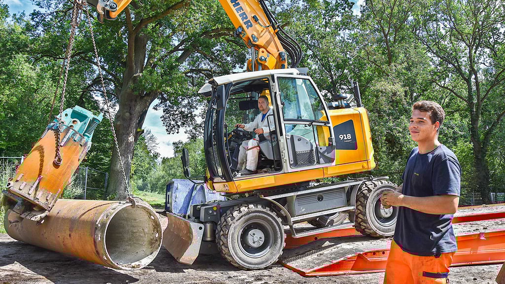Ein Bagger überquert in Kämkerhorst die Behelfsbrücke und transportiert einen Bohreimer sowie ein vier Meter langes Rohr auf der Baustelle.