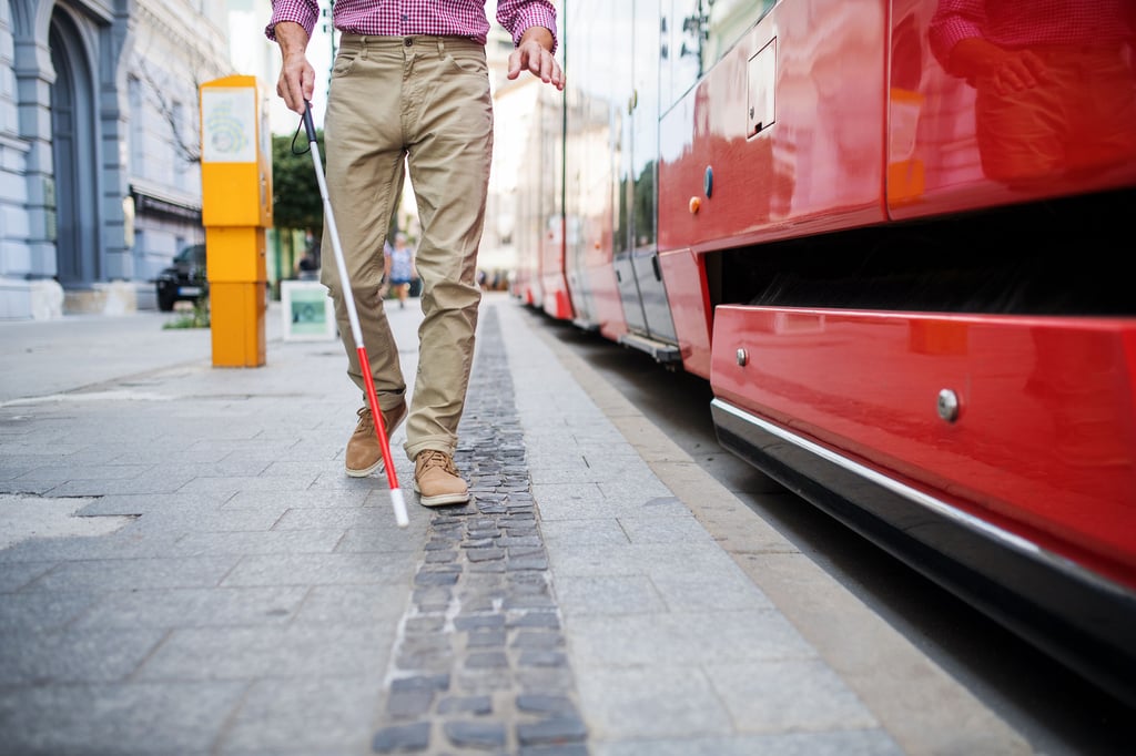 Ein sehbehinderter Mann geht mit Blindenstock an einem Verkehrsleitwegesystem entlang.