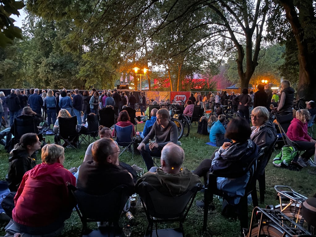 Genießen auch ohne Ticket das Konzert von Bryan Adams auf der Peißnitz: Tausende Zaungäste erleben Livemusik entspannt im Sitzen.