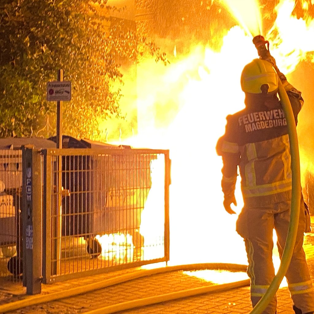 Ein Feuerwehrmann löscht die Flammen, die sich in der Nacht in Magdeburg Stadtfeld-Ost von einer Mülltonne auf mehrere Container ausgebreitet hatten. 