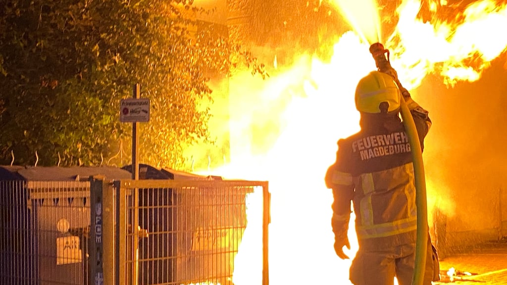 Ein Feuerwehrmann löscht die Flammen, die sich in der Nacht in Magdeburg Stadtfeld-Ost von einer Mülltonne auf mehrere Container ausgebreitet hatten.
