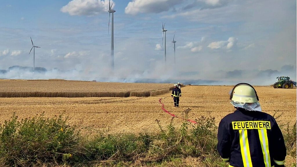 Feuerwehrleute und Landwirte im Einsatz: Gemeinsam versuchen sie, die Flammen auf dem brennenden Acker zu stoppen.