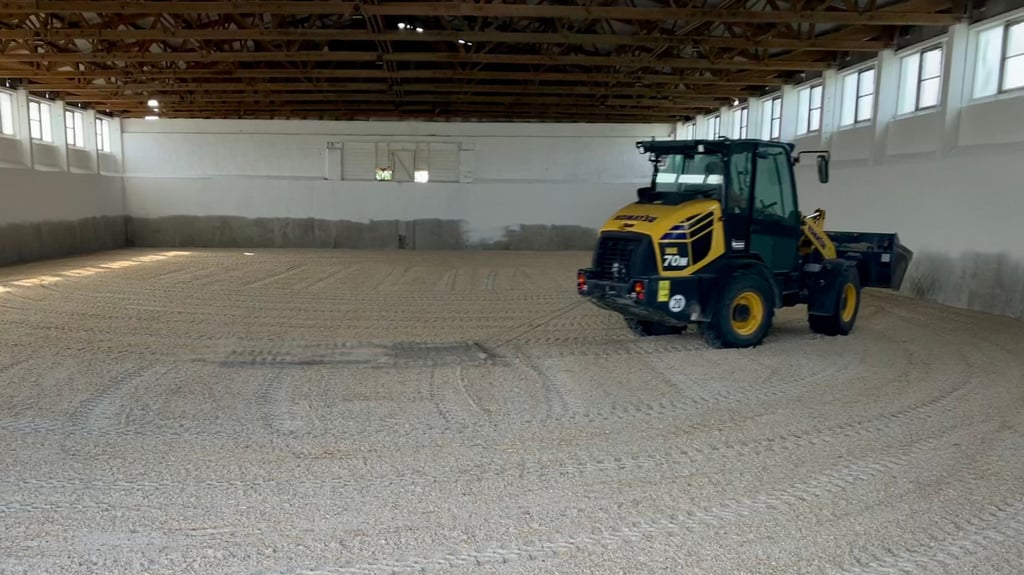 Der Radlader zieht ein Metallgitter über den neuen Reithallensand.