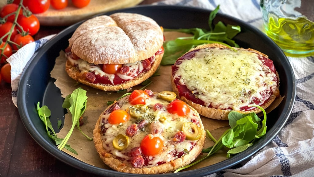 Ein rustikales Hamburgerbrötchen wird zur Pizzabasis, belegt mit Tomatenketchup, geschmolzenem Mozzarella und mediterranen Zutaten.