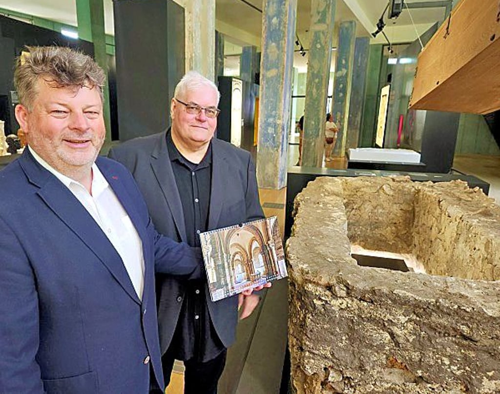 Die Fördervereinsvorsitzenden Thomas Nawrath und Rainer Kuhn präsentieren im Dommuseum in Magdeburg den Kalender vor dem vor genau 24 Jahren entdeckten steinernen Grab.