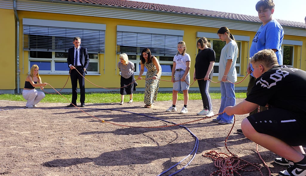 Wie bekommt man die kleinen gelbe Kugel aus der Mitte aus einem Kreis heraus, ohne den Kreis zu betreten und den Boden zu berühren? Eine Teambildungsmaßnahme für Sekundarschüler, an der aber auch Bildungsminister Jan Riedel zu knabbern hatte.
