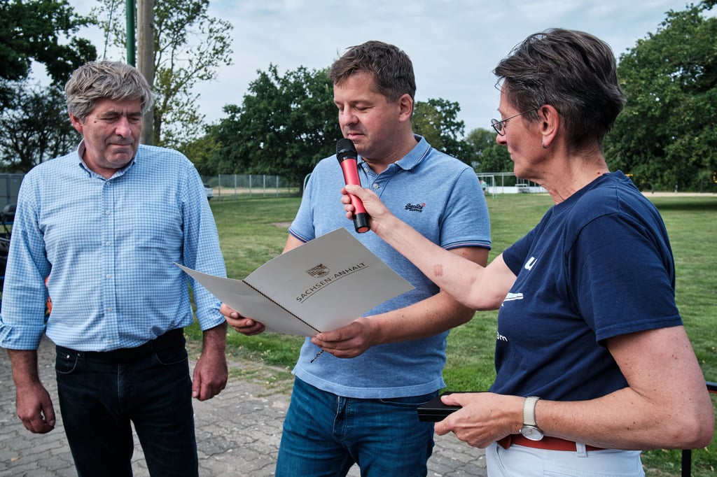 Fred Kitzing (l.) wird von Wirtschaftsminister Sven Schulze mit der Ehrennadel des Landes Sachsen-Anhalt geehrt. Das Mikrofon hält die CDU-Landtagsabgeordnete Anja Schneider.