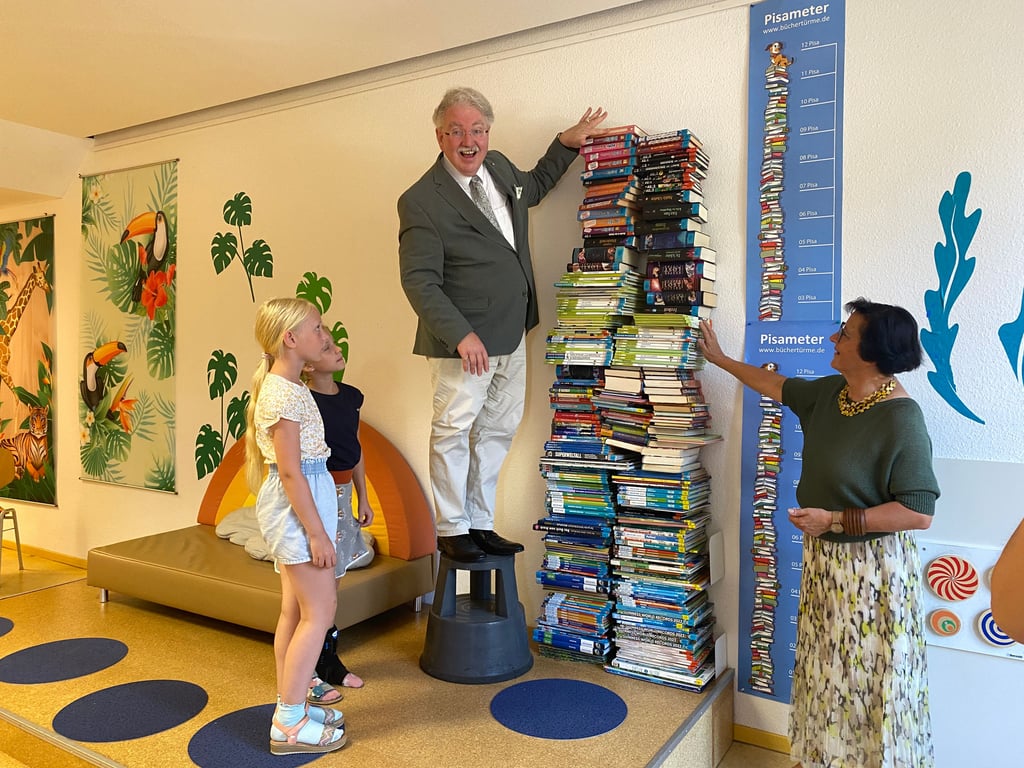 Gemeinsam mit Schülerinnen der Grundschule „Leipziger Straße“ setzt Stephen Stehli den Schlussstein des symbolischen Bücherturms in der Stadtbibliothek Magdeburg.