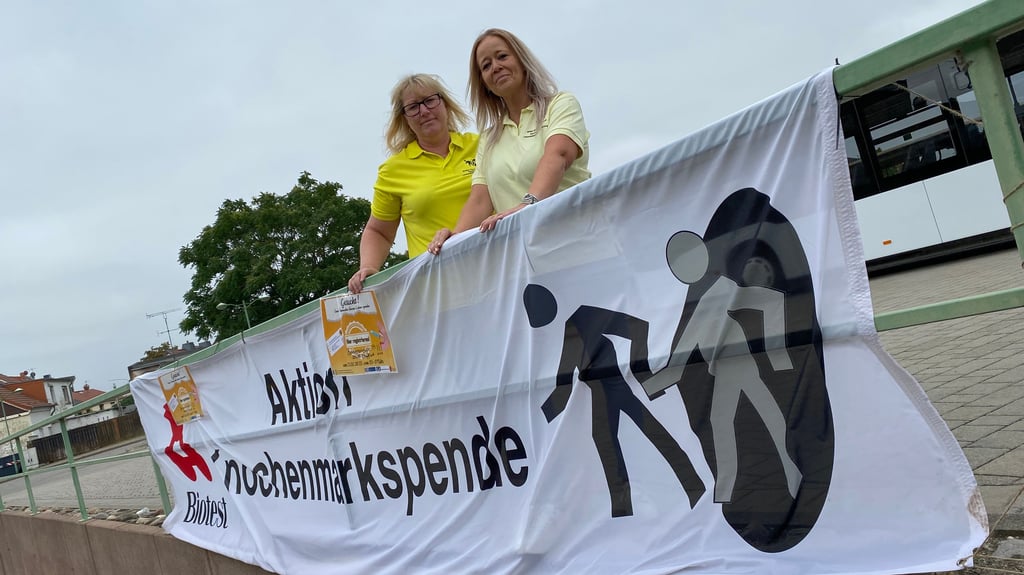 Jenny Stephan (links) und Eileen Hartmann-Balke, Mitarbeiter der Mediengruppe Magdeburg, laden mit einem Banner an Staßfurts Bahnhof zur Typisierung ein.