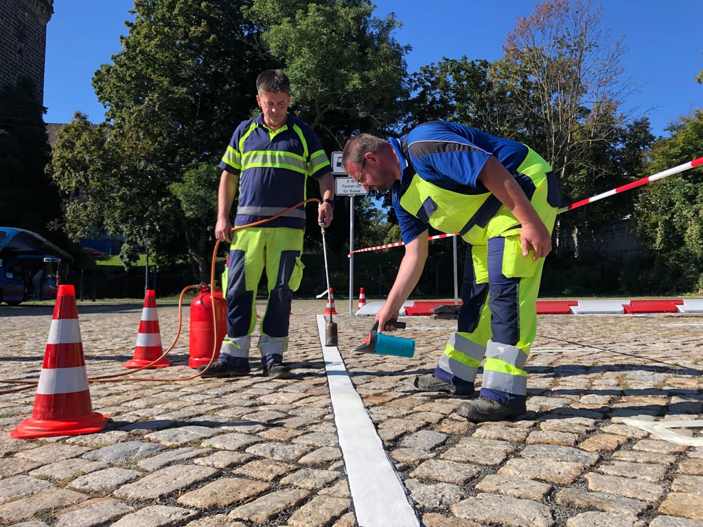 Martin Reinert (l.) und Björn Schumann vom städtischen Bauhof kleben die neue Markierung auf.