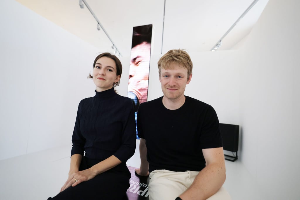 Die Künstler Ana Zibelnik (l) und Jakob Ganslmeier sitzen vor der von ihnen geschaffenen vier Meter hohen Videoskulptur zu neofaschistischem Körperkult auf TikTok in den Räumen des Museums für Zwangsarbeit vor der offiziellen Eröffnung des Kunstfests Weimar 2025.