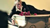 Helge Schneider liegt auf einem Klavier in einer Szene des Films „Helge Schneider - The Klimperclown“, der nun in der Mediathek zu sehen ist und am Mittwoch, 20.8., im Ersten gezeigt wird.