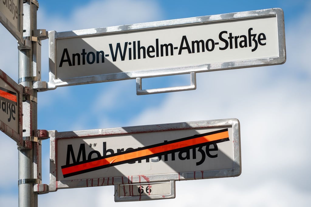 Ein Schild mit der Aufschrift „Anton-Wilhelm-Amo-Straße“ hängt über einem Schild, auf dem der Name „Mohrenstraße“ durchgestrichen ist.