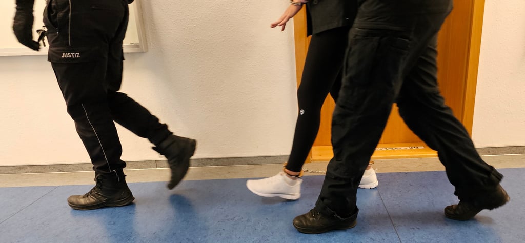 Die Angeklagte wird in Hand- und Fußfesseln in den Saal geführt.