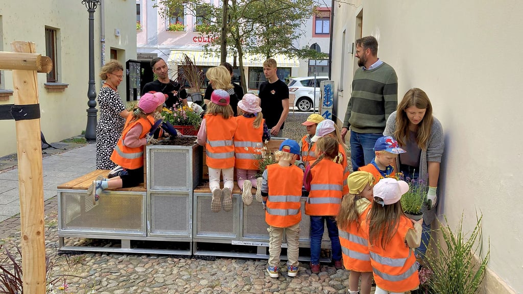 Kinder der Wittenberger „Kita an der Elbe“ helfen, diese neue Sitzgruppe in der Nähe des Ladens „Station 29“ zwischen Collegien- und Mittelstraße zu bepflanzen. Eine zweite Gruppe lädt in der Nähe des „Independent“ zum Verweilen ein.