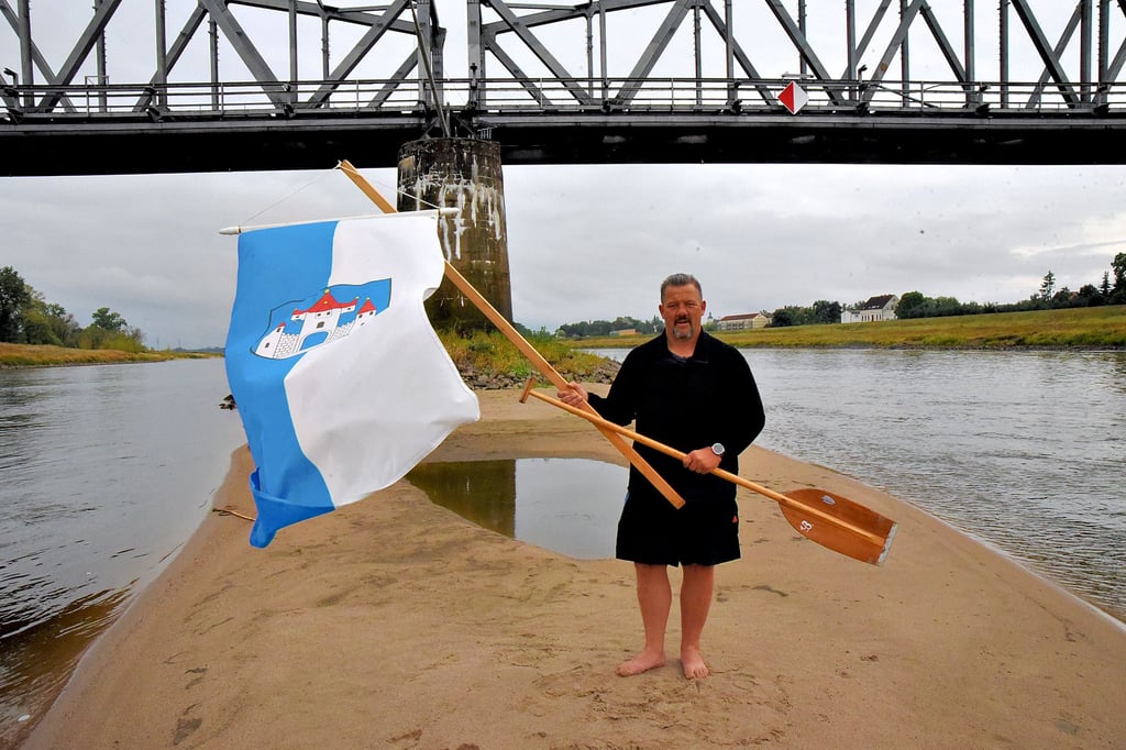 Peter Netzeband hat die Barbyer Flagge und ein Hilfspaddel in der Hand, um das sich eine besondere Geschichte rankt. Der Kanu-Abteilungsleiter ermöglichte mit dem Trainerboot diese Volksstimme-Reportage.