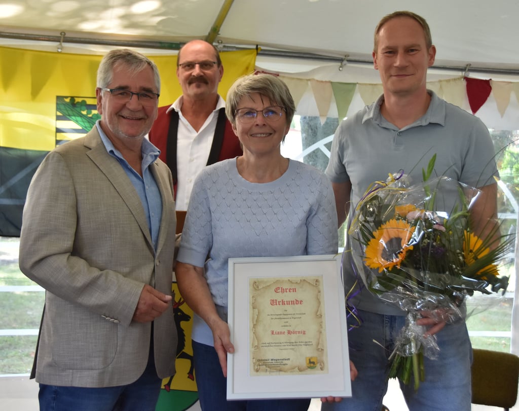 Liane Hörnig wird für ihr langjähriges Engagement in der Chronikkommission geehrt – mit Applaus, Blumen und einer Urkunde. Zu den Gratulanten zählen Bürgermeister Hubertus Nitzschke (l.), Hartmut Sonnenschein (2.v.l.) und Thomas Bruschies.