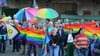 Menschen mit Regenbogenflaggen und -schirmen beteiligten sich an einer Kundgebung.