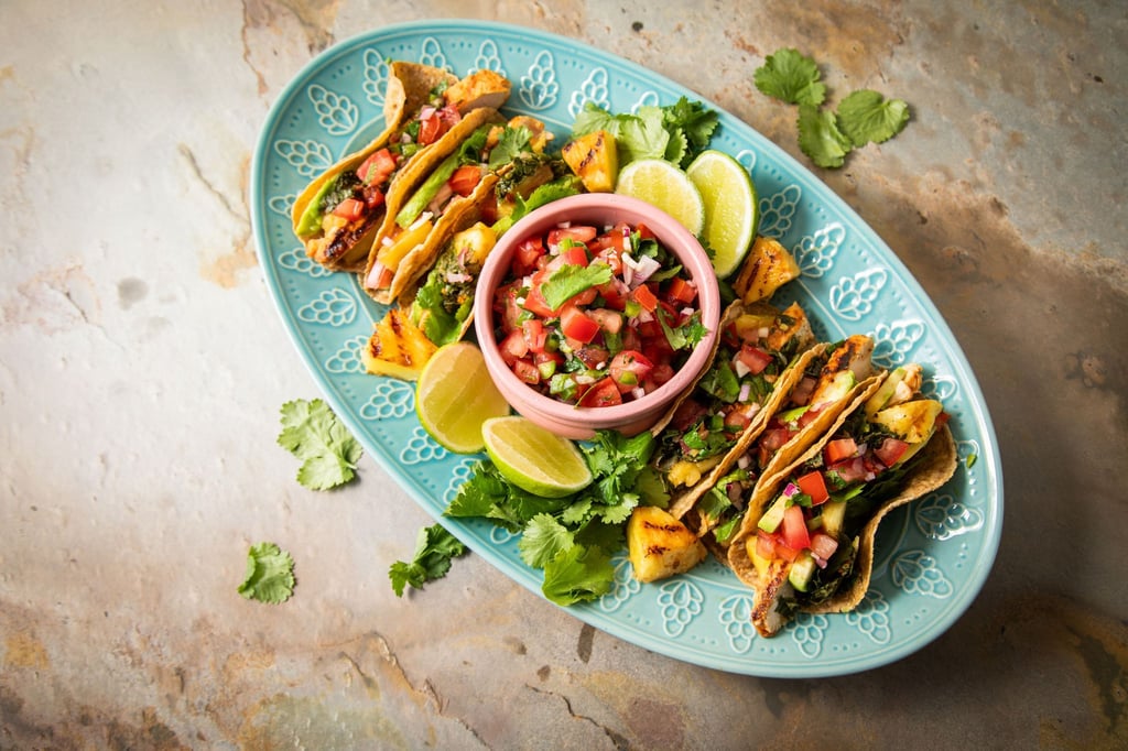 Richtig stilecht werden Hähnchen-Tacos erst mit Zugaben wie der mexikanische Tomatensalsa „Pico de Gallo“, argentinischer Kräutersauce „Chimichurri“, Avocado, gegrillter Ananas, Koriander und Limetten.