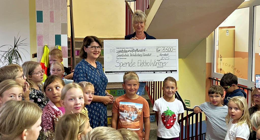 Geschäftsführerin Marion Würkner (auf der Treppe) kam mit einem symbolischen Scheck in die Farnstädter Grundschule, den sie an Schulleiterin Dorothea Siegert (links daneben) sowie an Schüler und Lehrer überreichte.