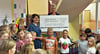 Geschäftsführerin Marion Würkner (auf der Treppe) kam mit einem symbolischen Scheck in die Farnstädter Grundschule, den sie an Schulleiterin Dorothea Siegert (links daneben) sowie an Schüler und Lehrer überreichte. 