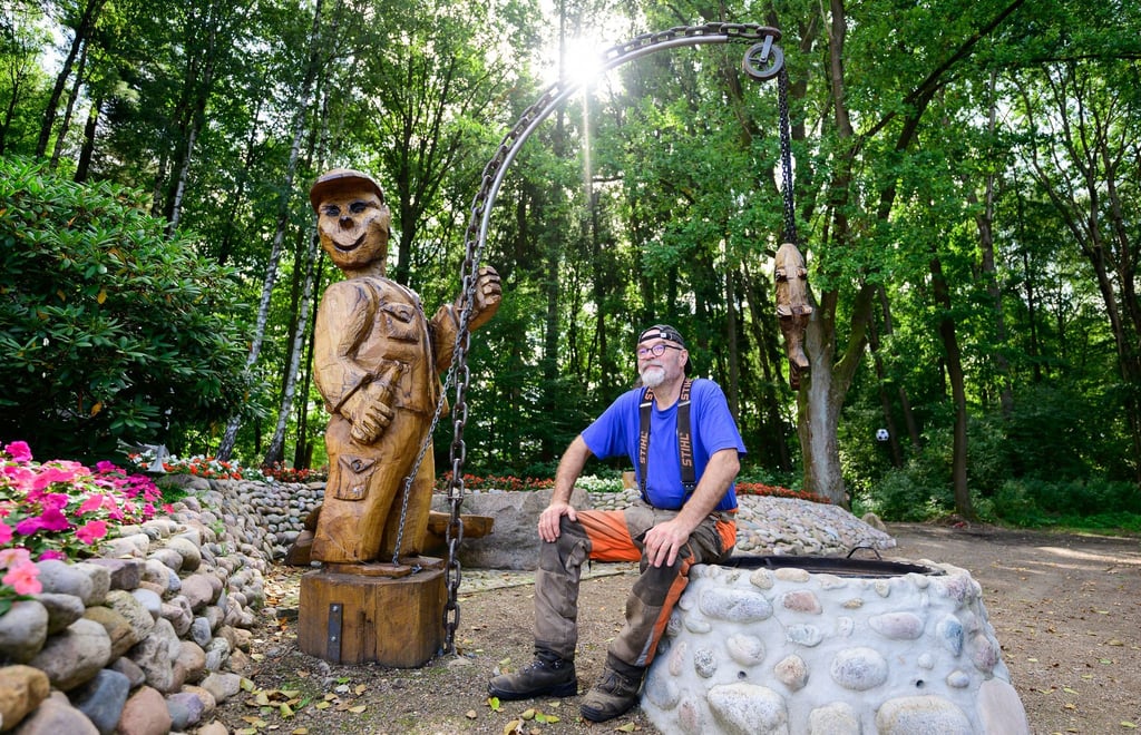 Motorsägenkünstler Andree Löbnitz neben einer Holzskulptur, die er aus einem Holzstamm schnitzte.