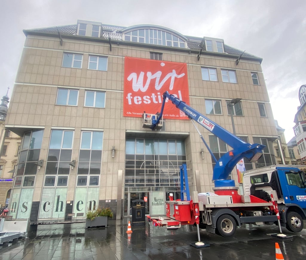 Ein riesiges Transparent am Kaufhof weist auf das „Wir“-Festival hin, das am Sonntag mit einer spektakulären Mitmach-Aktion auf Halles Marktplatz eröffnet wird.