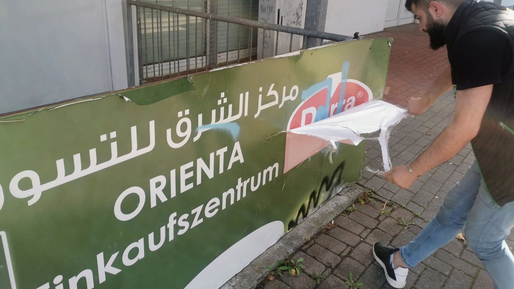 Ein Mitarbeiter des Orienta Supermarkts in Neu-Olvenstedt klebt ein Hakenkreuz ab. Es wurde mit blauer Grafitti-Farbe an das Werbebanner gesprüht.
