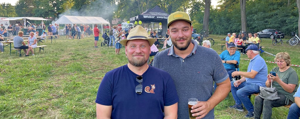 Vereinsvorsitzender Tobias Kronfeldt (links) und Kuhbingo-Gewinner Dennis Roussiere. Im Hintergrund die Besucherwiese, auf der zahlreiche Gäste das Schauspiel verfolgt hatten. Die Rinderweide selbst war in 400 kleine Quadrate aufgeteilt worden.