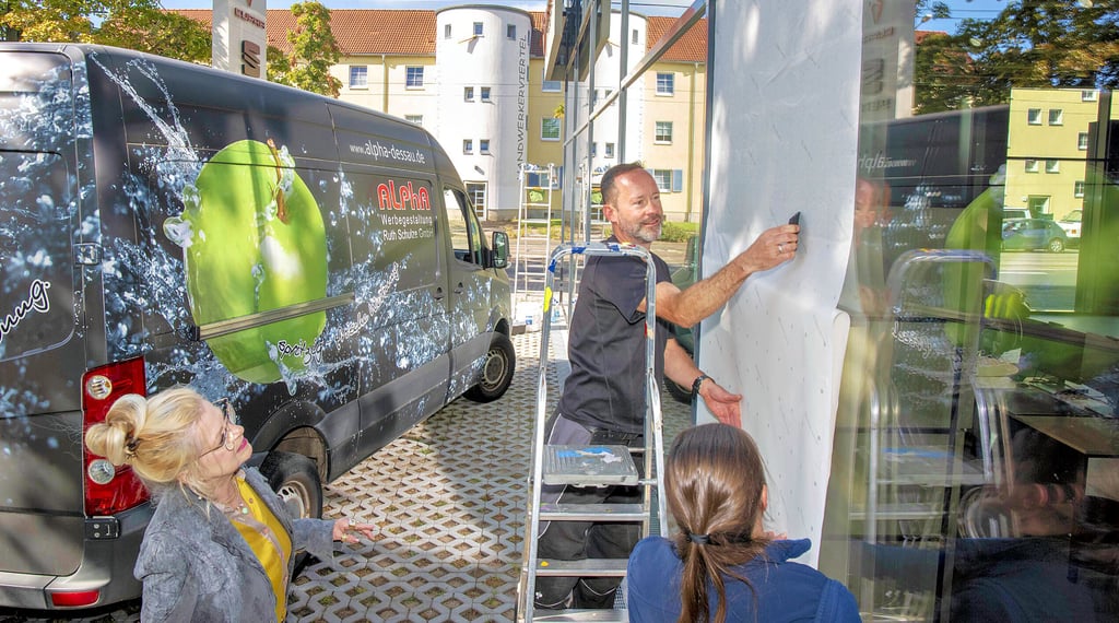 Die Firma Alpha Werbung von Ruth Schulze (l.) beklebt beim Autohaus Feser Heise die Außenscheiben mit einer neuartigen Vogelschutzfolie. Im Bild: Maik Wagner und Anne Minz.