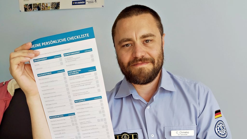 Constantin Chmelka, Ortsverbandschef des Technischen Hilfswerks Salzwedel, hält eine Checkliste des Bundesamtes für Katastrophenschutz  zum Selbstschutz für Bürger in die Höhe.