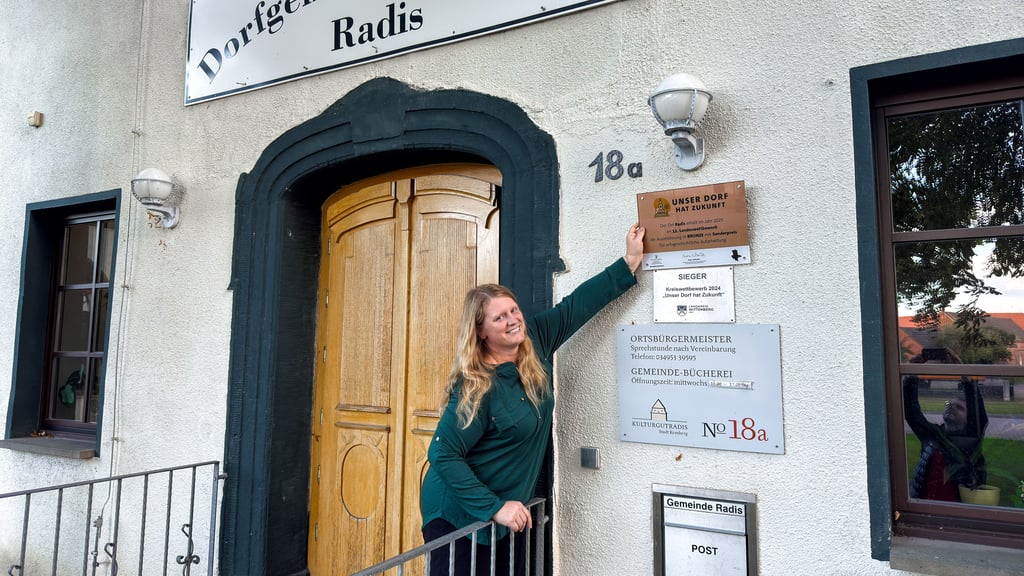 Ein Platz ist schon reserviert: Ortsbürgermeisterin Sandra Mannel probiert aus, wo die bronzefarbene Wettbewerbsplakette künftig hängen soll.