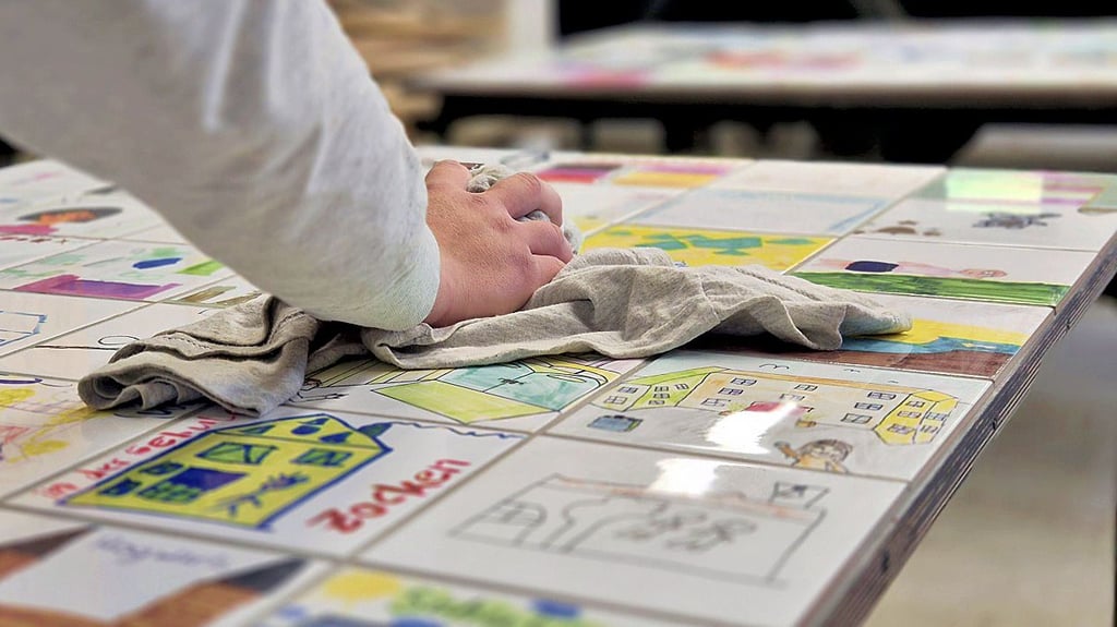 Mit Kinderbildern bedruckte Fliesen wurden auf Siebdruckplatten geklebt und verfugt. Noch einmal drüber gewischt und dann können sie in Stendal ausgestellt werden.